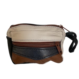 May include: A small, rectangular leather coin purse with a zipper closure. The purse is made of cream, black, and brown leather panels. It has a brown zipper and a black wrist strap.