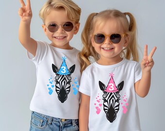 May include: Two children wearing white t-shirts with a zebra head design. The zebra has a party hat with the number 3. Blue and pink hearts surround the zebra. Both children are wearing sunglasses and making a peace sign.