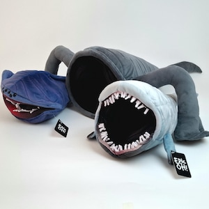 May include: Three plush monster toys in blue and gray. The toys have large open mouths with white teeth and red accents. Each toy has a tag that says "Epic Oh!".