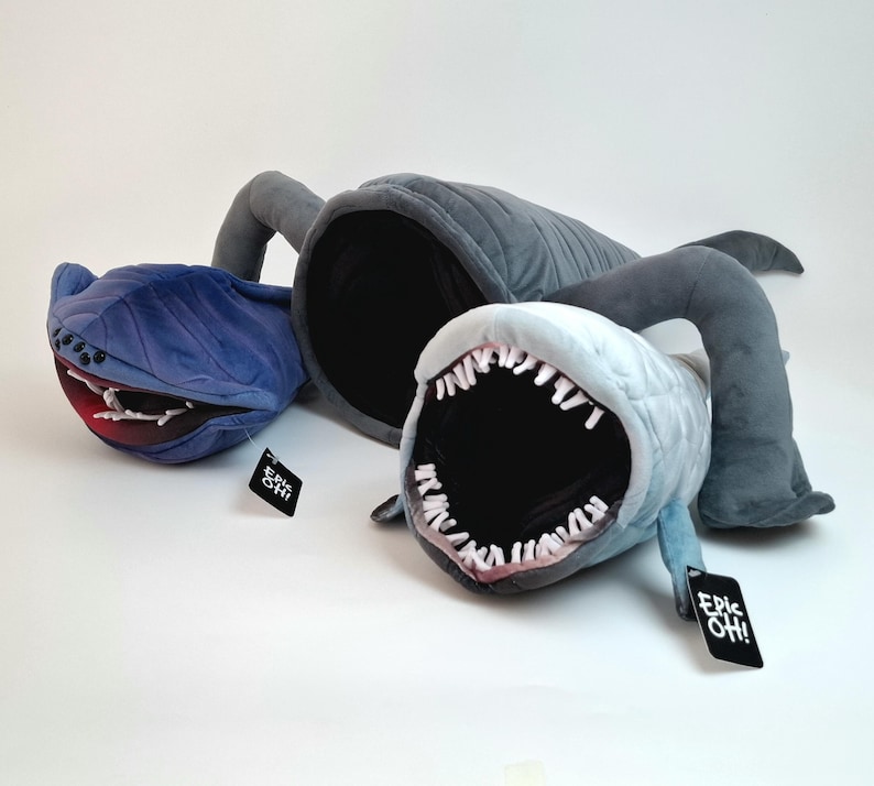May include: Three plush monster toys in blue and gray. The toys have large open mouths with white teeth and red accents. Each toy has a tag that says "Epic Oh!".