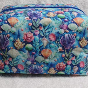 May include: A rectangular fabric pouch featuring a vibrant underwater-themed print. The design displays various seashells, coral, and aquatic plants in shades of blue, purple, pink, and orange against a deep blue background with a blue zipper.