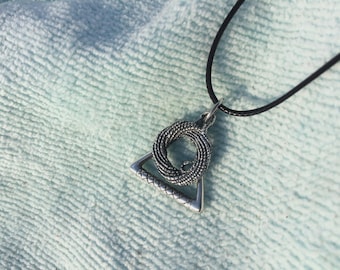 May include: Silver-toned pendant necklace featuring a geometric design. The pendant combines a triangular shape with a circular, woven element. The necklace has a black cord, and the pendant is displayed on a light blue textured surface.