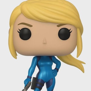 May include: A Funko Pop vinyl figure of Samus Aran from the Metroid video game series. The figure features a blonde-haired character in a blue and purple armored suit, holding a blaster. The figure stands on a black base.