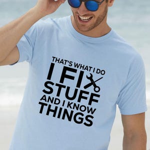 Könnte beinhalten: Hellblaues T-Shirt mit dem Text "THAT'S WHAT I DO I FIX STUFF AND I KNOW THINGS" in Schwarz. Das T-Shirt zeigt einen Schraubenschlüssel und eine Schere. Die Person auf dem Bild trägt eine Sonnenbrille.