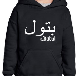 Può includere: Felpa con cappuccio nera con tasca frontale. La felpa presenta il nome "Batul" in caratteri arabi bianchi sopra la traslitterazione inglese del nome.