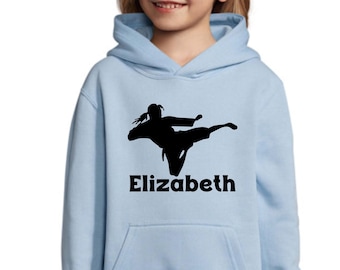 Puede incluir: Sudadera azul claro con una silueta negra de una persona realizando una patada de artes marciales. El nombre "Elizabeth" está impreso en letras negras debajo del gráfico. La sudadera tiene un bolsillo delantero y una capucha.