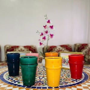 Peut inclure: Plusieurs pots de fleurs en céramique colorés, bleus, verts, roses, oranges, jaunes et rouges. Les pots sont disposés sur une table en mosaïque, avec une orchidée blanche et violette en arrière-plan.