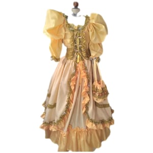 Może przedstawiać: Suknia w stylu vintage w odcieniach żółci i brzoskwini, z bufiastymi rękawami, dopasowanym stanikiem i obszerną spódnicą. Suknia jest ozdobiona złotymi wykończeniami i falbanami oraz zawiera pasującą małą torebkę. Suknia jest prezentowana na manekinie.