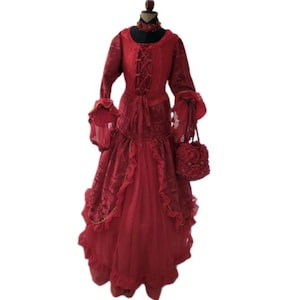 Może przedstawiać: Czerwona sukienka w stylu wiktoriańskim z długimi rękawami, gorsetem sznurowanym i warstwową spódnicą. Sukienka posiada falbanki i jest połączona z pasującą torebką i chokerem. Zestaw jest prezentowany na manekinie.