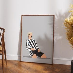 Puede incluir: Un cuadro enmarcado con una ilustración estilizada de un futbolista con una camiseta a rayas blancas y negras, celebrando. La obra de arte tiene un estilo minimalista con un fondo gris y un marco marrón.