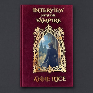 May include: A hardcover book titled Interview with the Vampire by Anne Rice. The cover is deep burgundy with a velvet-like texture and features gold foil lettering. A central gold filigree frame surrounds an illustration of a figure in a dark coat.