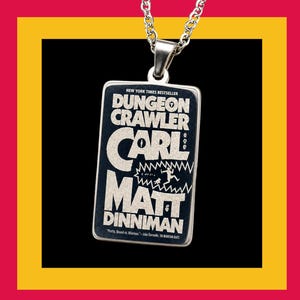 May include: A rectangular silver-toned metal pendant on a chain featuring a black face with white text that reads Dungeon Crawler Carl by Matt Dinniman, including a graphic of a figure running from a large mouth with sharp teeth.
