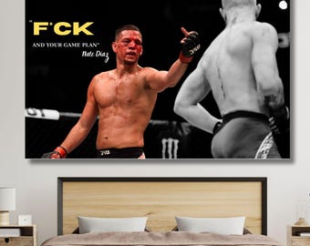 May include: A framed print featuring a mixed martial arts scene. The image shows two fighters, one in color and the other in black and white. Text on the print reads "F*CK AND YOUR GAME PLAN" and "Nate Diaz". The print is displayed above a bed.