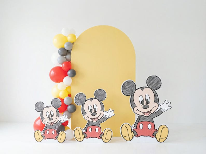 Puede incluir: Un tel&oacute;n de fondo de arco amarillo con tres recortes de Mickey Mouse frente a una guirnalda de globos. Los recortes de Mickey Mouse son negros, rojos y amarillos. La guirnalda de globos incluye globos rojos, amarillos, grises y blancos.