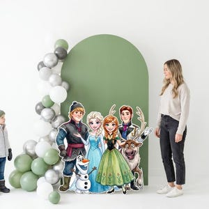 May include: A party scene featuring cardboard cutouts of characters from the animated film "Frozen", including Anna, Elsa, Kristoff, and Olaf. A young child and an adult woman are also present. A balloon arch in shades of green, silver, and white decorates the background.