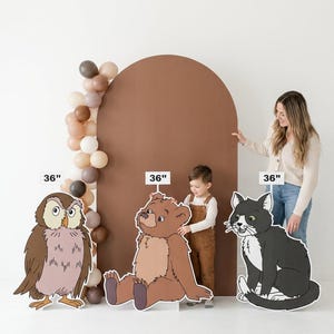 May include: Cardboard cutouts of an owl, bear, and cat, each approximately 91 cm tall. The owl is brown and pink, the bear is tan, and the cat is black and white. A brown arch and balloon garland are in the background.