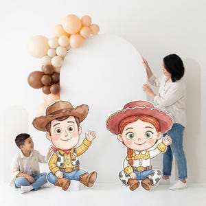 May include: A party scene featuring cardboard cutouts of cartoon cowboy characters, a balloon arch in neutral tones, and a white backdrop. A woman and a child are interacting with the decorations. The characters are wearing cowboy hats and outfits.
