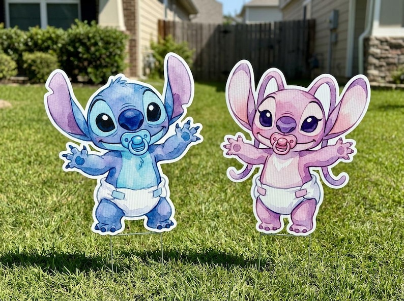 May include: Two decorative yard signs featuring cartoon characters in diapers with pacifiers. One character is blue with large ears and arms outstretched, while the other is pink with similar features. Both figures are standing on metal stakes.