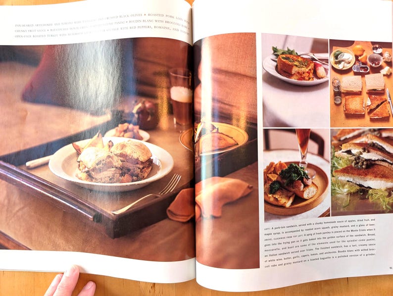 May include: A spread of food items, including sandwiches, on a wooden tray and plates. A sandwich on a white plate sits on a wooden tray. Other plates and glasses are also visible, with a fork and a napkin.