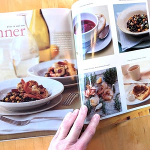 May include: A magazine spread featuring various dinner dishes. The page includes images of shrimp with a dark grain, a bowl of soup, and a slice of cake. The text "dinner" is visible in pink.