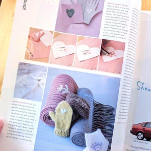 May include: A magazine page featuring various craft projects. The page includes images of knitted items, including a pink scarf with a snowflake design, a yellow mitten, and rolled-up socks. There are also paper hearts and hand-shaped cutouts.