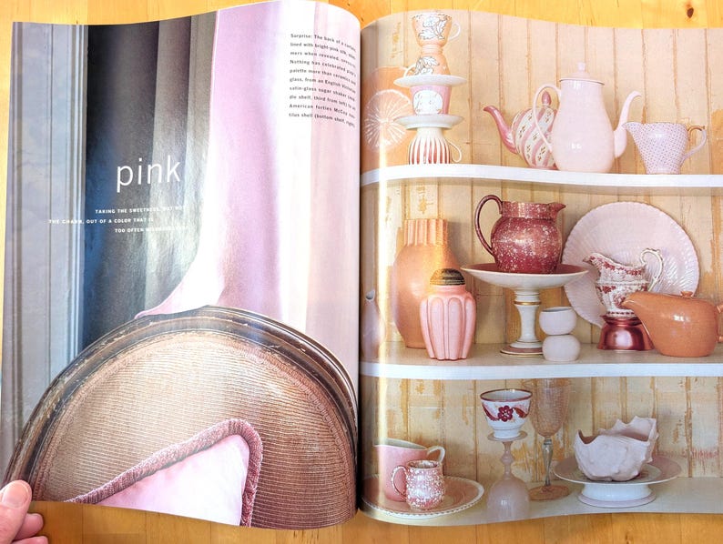 May include: A magazine spread featuring a collection of pink and peach-colored teacups, teapots, pitchers, and decorative vases displayed on white shelves. The word "pink" is visible on the left page. The overall aesthetic is vintage and elegant.