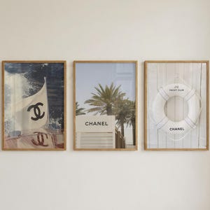 May include: Three framed wall art prints featuring Chanel branding. The left print shows a boat flag with the Chanel logo. The centre print displays a palm tree and a building with the text CHANEL. The right print shows a life buoy with J12 YACHT CLUB and CHANEL.