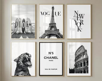 May include: A set of six black and white wall art prints in gold frames. The prints feature surfboards with the text DIOR, the Eiffel Tower with VOGUE, the text NEW YORK City, a leopard, a Chanel N°5 perfume label, and the Roman Colosseum.