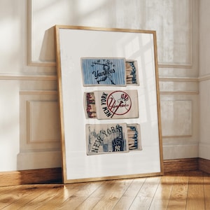 Puede incluir: Una lámina artística vertical enmarcada que muestra tres cajas de cerillas con temas de béisbol de los New York Yankees. La caja superior muestra un bateador, la central un logotipo de béisbol con el texto New York Yankees y la inferior la Estatua de la Libertad.