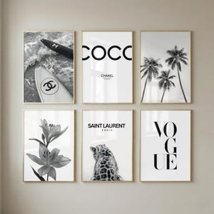 May include: A set of six framed wall art prints in black and white. The images feature surfboards with Chanel logos, the text COCO CHANEL, palm trees, a lily flower, a leopard with the text SAINT LAURENT PARIS, and the word VOGUE in bold letters.