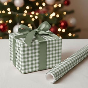 May include: A wrapped gift box with a green and white gingham pattern, tied with a matching green satin ribbon and bow. A roll of coordinating wrapping paper is next to the gift. The background features a Christmas tree with lights and ornaments.