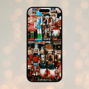 May include: A phone screen displays a collection of colorful wooden nutcrackers. The nutcrackers are of various sizes and designs, including soldiers, gnomes, and other festive characters. The background is blurred with bokeh lights.