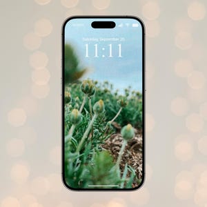 May include: A smartphone displays a nature-themed wallpaper with green plants and flower buds. The screen shows the date as Saturday, September 20, and the time as 11:11 in white text. The phone has a black border and is set against a blurred background.