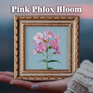 May include: A square framed oil painting featuring a cluster of pink phlox flowers against a light blue background. The ornate gold frame has a textured, repeating leaf pattern. The text "Pink Phlox Bloom" is printed in white above the frame.