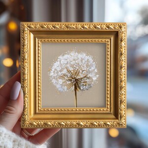 May include: A square painting of a white dandelion seed head on a beige background, encased in an ornate, textured gold frame. The artwork features thick, layered paint strokes that create a three-dimensional effect for the flower petals.