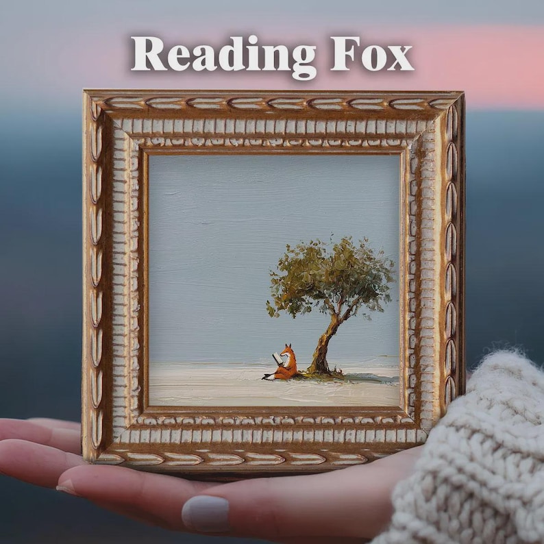 May include: A framed miniature painting titled "Reading Fox." The artwork depicts an orange fox reading a book under a tree. The frame is gold with ornate detailing. The background is a soft blue and white landscape.