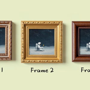 May include: Three framed art prints featuring an astronaut on a lunar surface holding a flower. Each print is in a different style frame: ornate gold, dark brown, and a light brown with a decorative border. The text "Frame 1", "Frame 2", and "Frame 3" is below each.