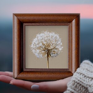May include: A square painting of a white dandelion seed head with textured paint strokes on a light beige background, encased in a polished dark brown wooden frame with a beveled edge and a visible wood grain pattern throughout the frame.
