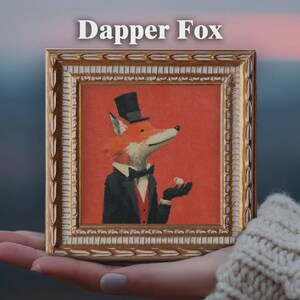 May include: A framed painting featuring a fox in a tuxedo and top hat, holding a small cup. The artwork has a red background and is labeled "Dapper Fox" in white text. The frame is gold-colored with ornate detailing.