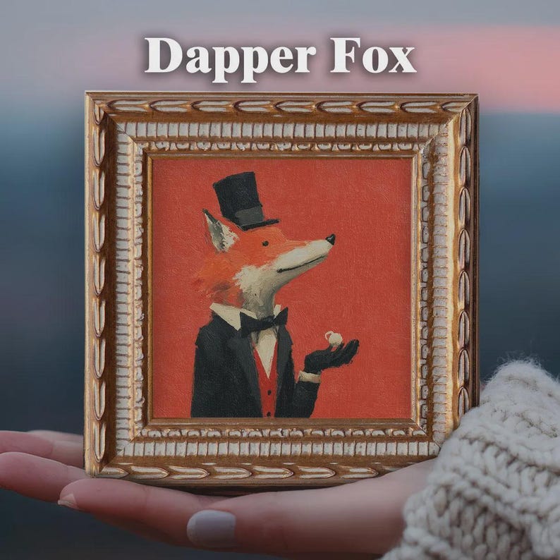 May include: A framed painting featuring a fox in a tuxedo and top hat, holding a small cup. The artwork has a red background and is labeled "Dapper Fox" in white text. The frame is gold-colored with ornate detailing.