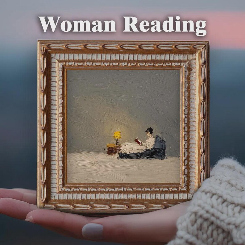 May include: A framed painting with the text "Woman Reading" at the top. The painting depicts a person in a white dress reading under a yellow lamp. The frame is gold with ornate detailing.