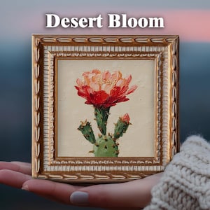 May include: A square oil painting titled Desert Bloom featuring a vibrant red and orange cactus flower on a light beige background, encased in an ornate gold frame with a textured, carved border pattern and a white inner trim detail.