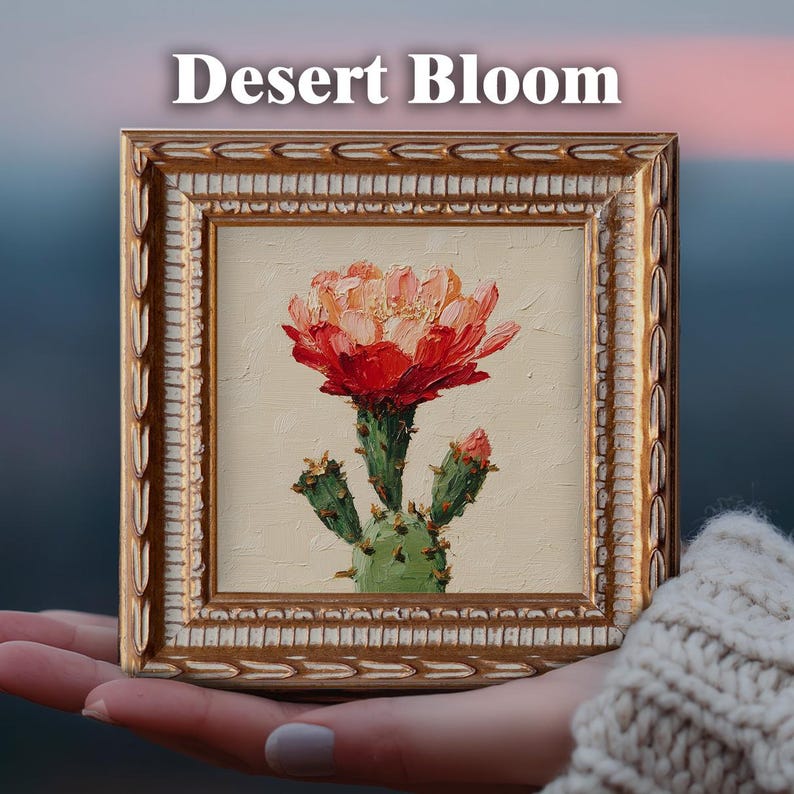 May include: A square oil painting titled Desert Bloom featuring a vibrant red and orange cactus flower on a light beige background, encased in an ornate gold frame with a textured, carved border pattern and a white inner trim detail.
