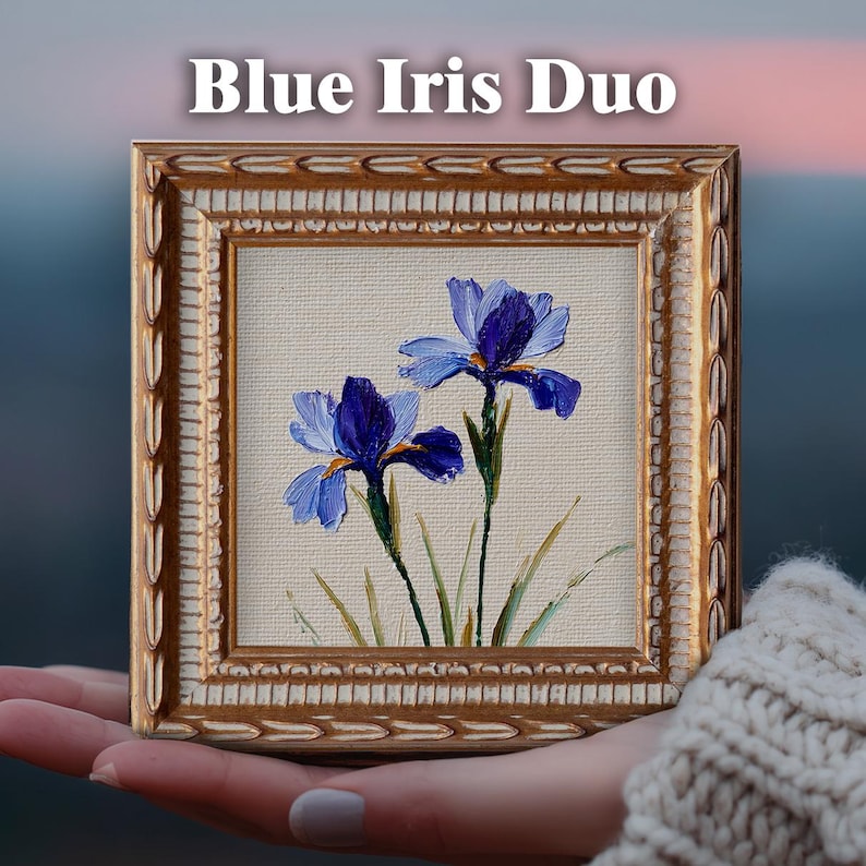 May include: A small square painting titled Blue Iris Duo featuring two blue iris flowers with green stems on a cream background, encased in an ornate gold frame with a textured border. The artwork displays visible brushstrokes and impasto texture.