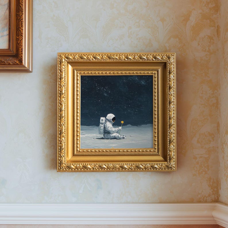 May include: A framed painting depicts an astronaut seated on a lunar surface, holding a yellow flower. The artwork is set against a dark, starry sky. The painting is enclosed in a gold ornate frame, adding a touch of elegance to the space-themed art.
