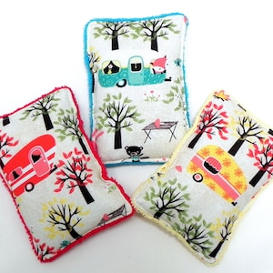 Op de afbeelding: Drie kleurrijke stoffen theedoeken met een kampeerthema. Elke theedoek heeft een camper van een andere kleur met een witte achtergrond en zwarte bomen. De theedoeken hebben een rode, blauwe en gele rand.