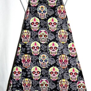 May include: An ironing board cover featuring a repeating pattern of colorful sugar skull designs on a black background. The skulls have intricate floral and geometric details in various colors, including pink, orange, and green.