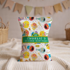 May include: A white party favor bag featuring Sesame Street characters like Elmo and Big Bird, with confetti and party hats. The bag has a green label that reads "Charlie's Second Birthday" with the number 123 above it. The bag is on a white, textured surface.