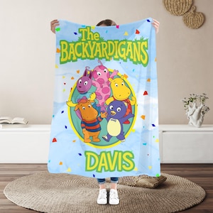 May include: A light blue fleece blanket featuring The Backyardigans characters in a central yellow circle. The text reads The Backyardigans at the top and Davis at the bottom. The background is decorated with scattered colorful confetti shapes.
