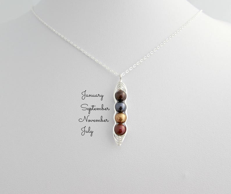 Puede incluir: Collar de plata con un colgante en forma de vaina de guisantes, que contiene cuatro cuentas de colores: marr&oacute;n, gris oscuro, dorado y rojo. Las palabras "Enero, Septiembre, Noviembre, Julio" est&aacute;n escritas a la izquierda.